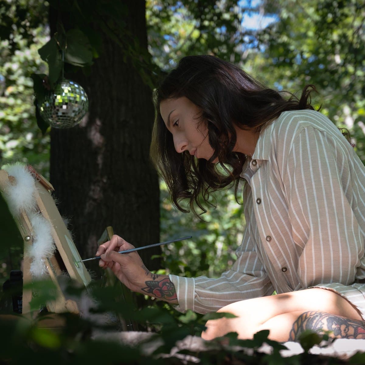 Julie Jewelz painting a small canvas on a wooden easel outdoors near Elyria, Ohio